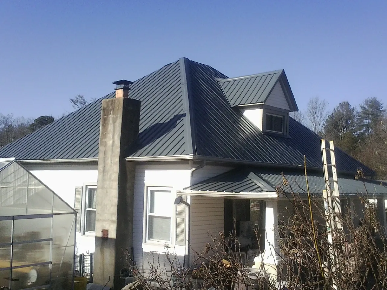 Dark blue standing seam metal roof on a white farmhouse with dormer — Slate & Tile Roof Repair by Roofing Brothers in Argyle