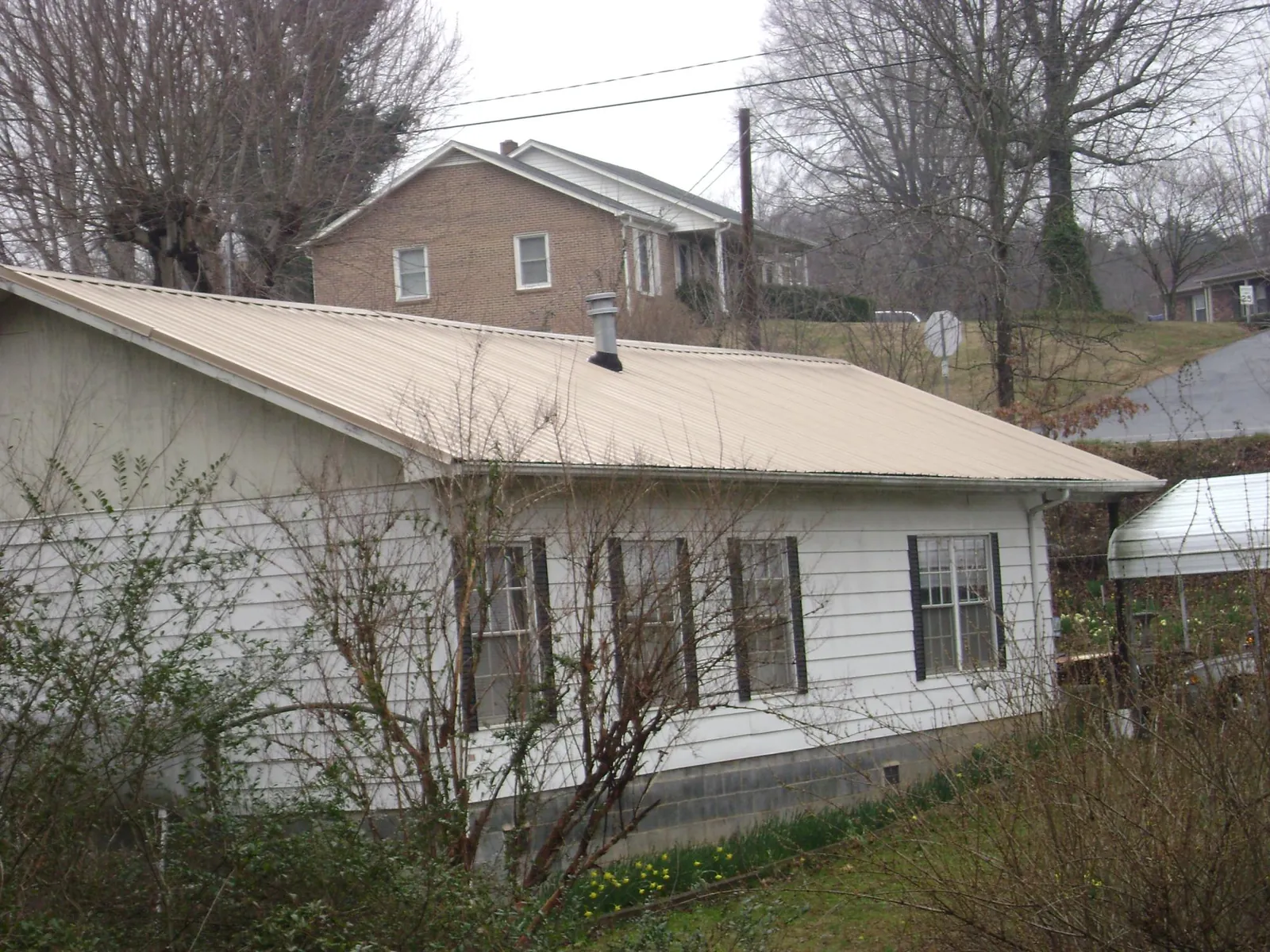 Tan metal roof on a white sided house set into a hillside — Commercial Roofing by Roofing Brothers in Argyle